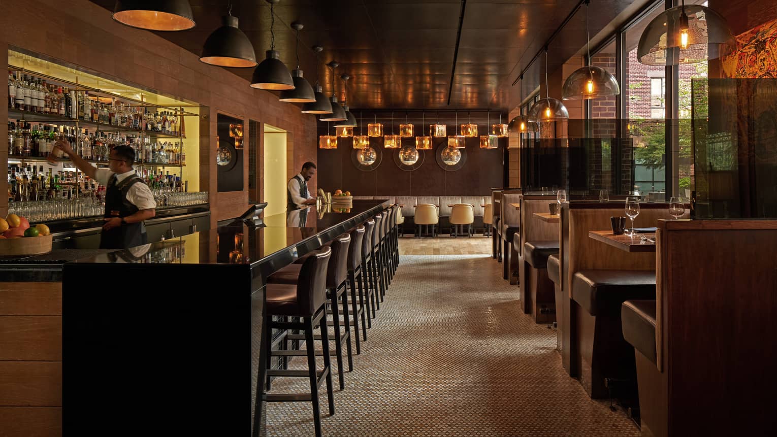 A dimly lit bar with dark wood stools and booths.