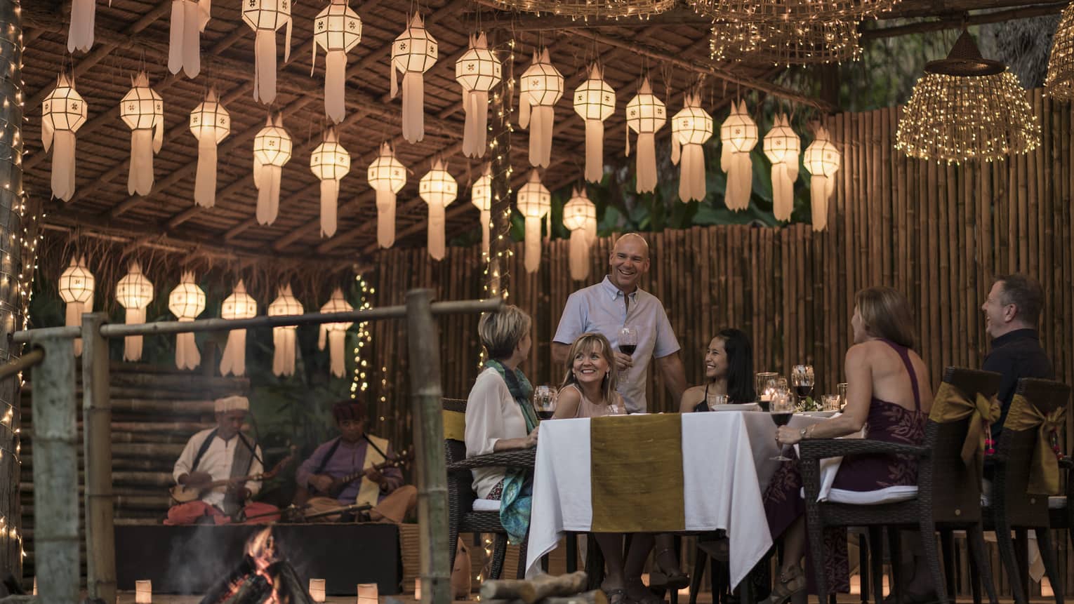A group of people sitting at a table enjoying a meal in outdoor pavilion decorated with lanterns