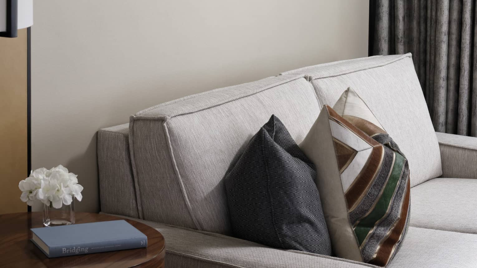 Cream loveseat, patterned accent pillows, wooden side table, wall art trio, grey curtains