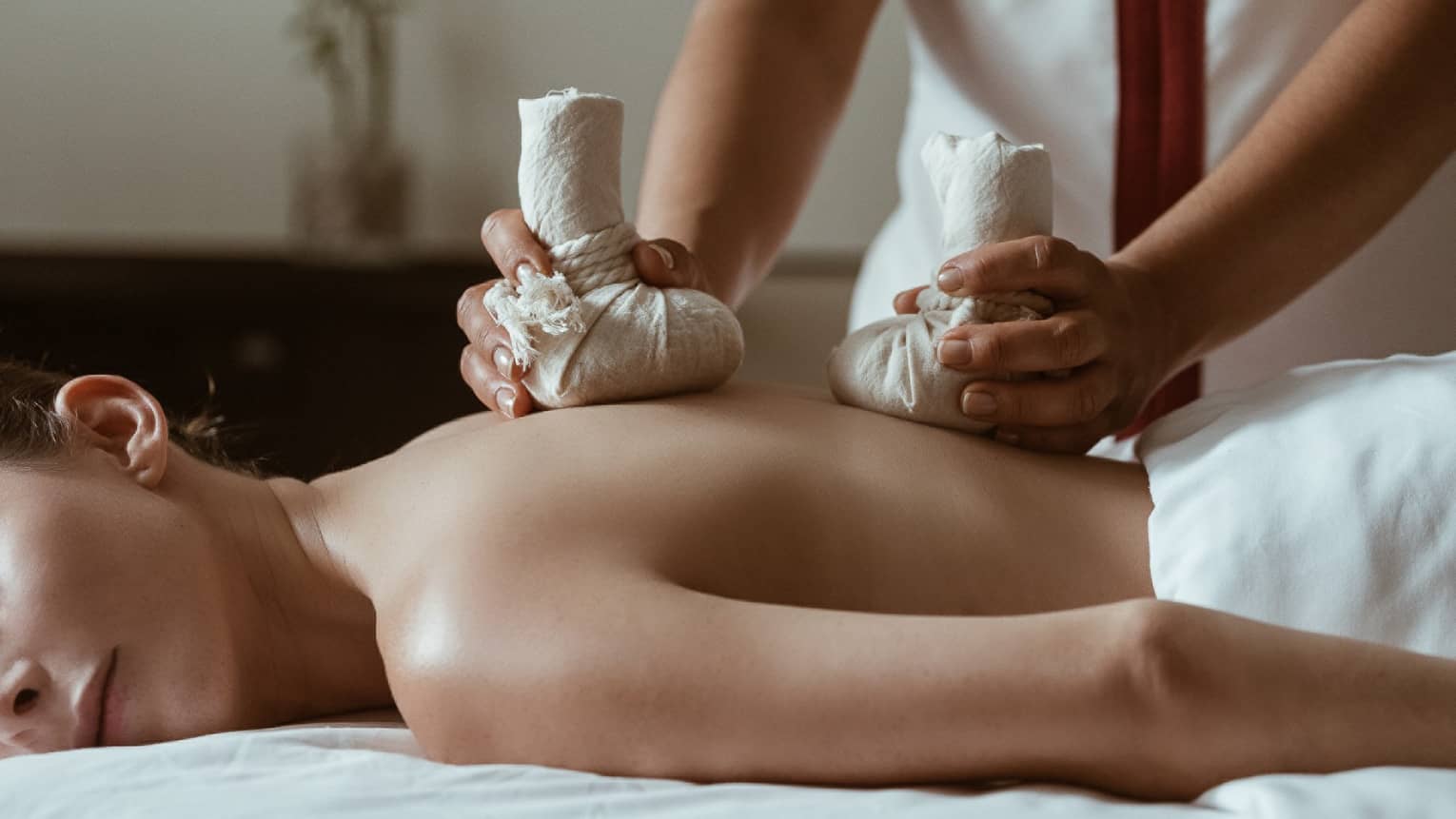 A woman being massaged by heavy stones in cloth bags.