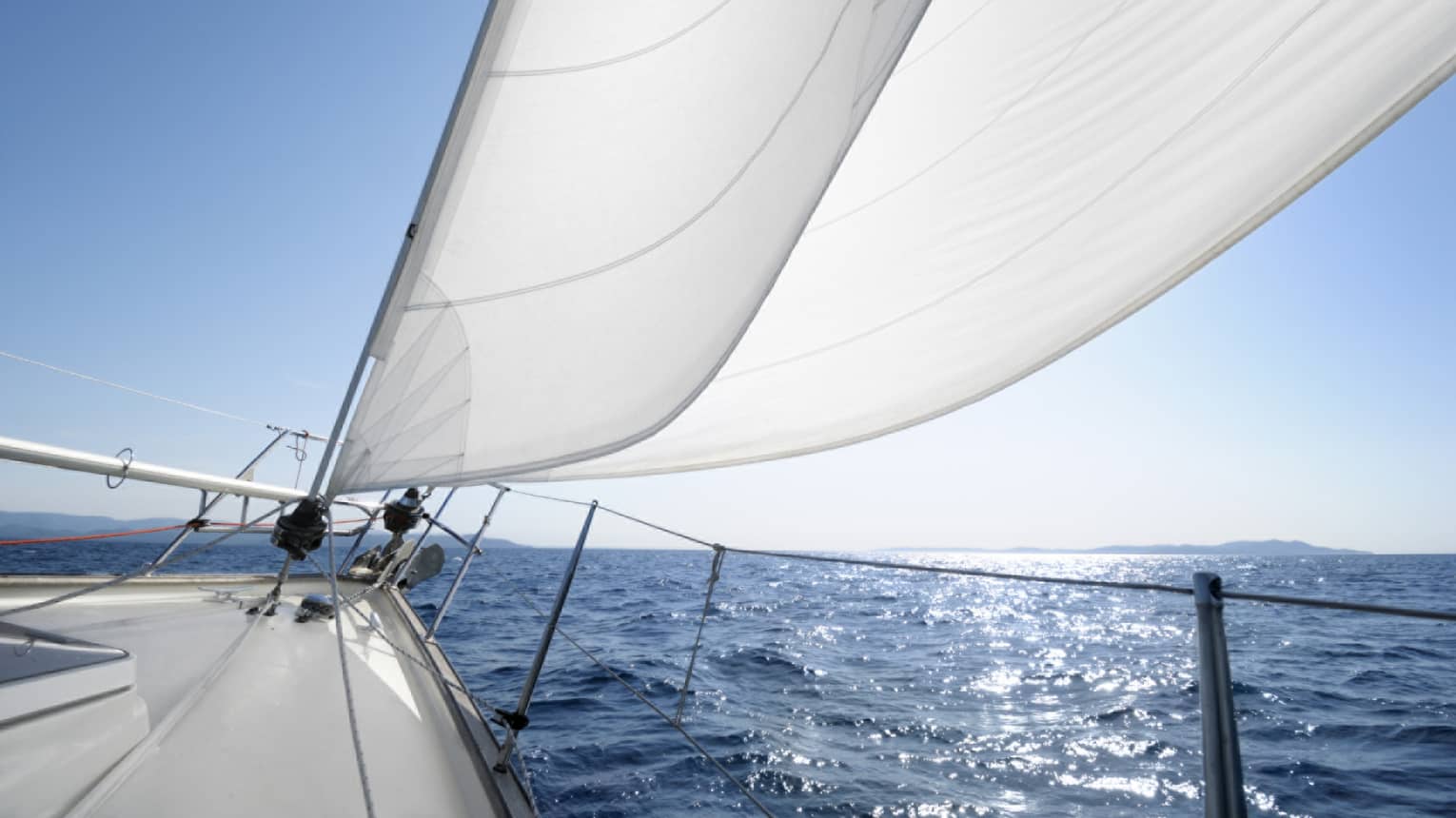 Close-up of white sails on yacht, blue ocean in background
