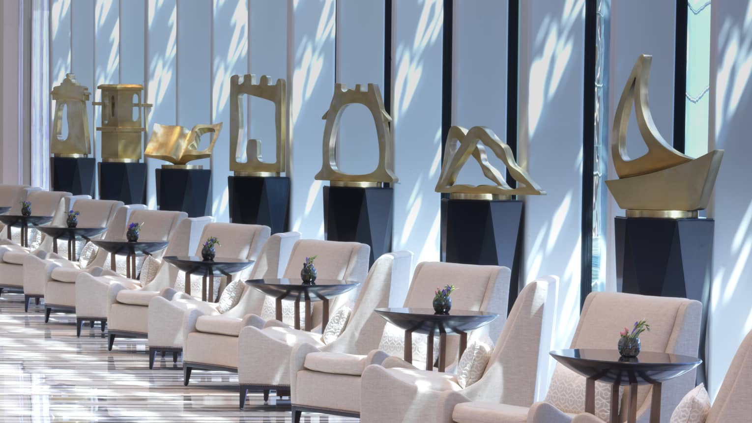 Several golden sculptures are on pedestals in a long white marble hallway. 