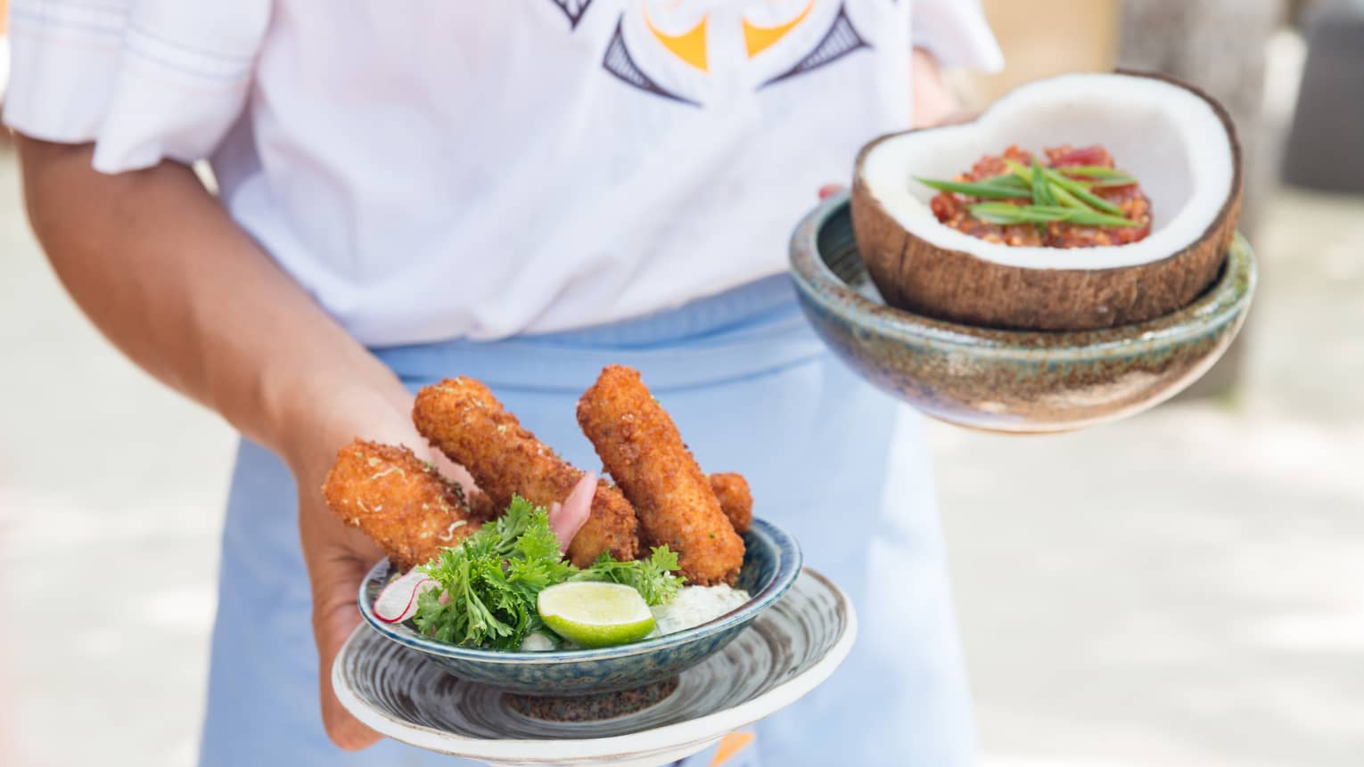 Hotel staff holds appetizers in small bowl and coconut shell