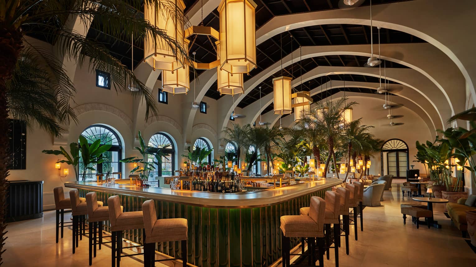 Evening view of Le Sirenuse indoor Champagne bar, stools and palms lining white bar