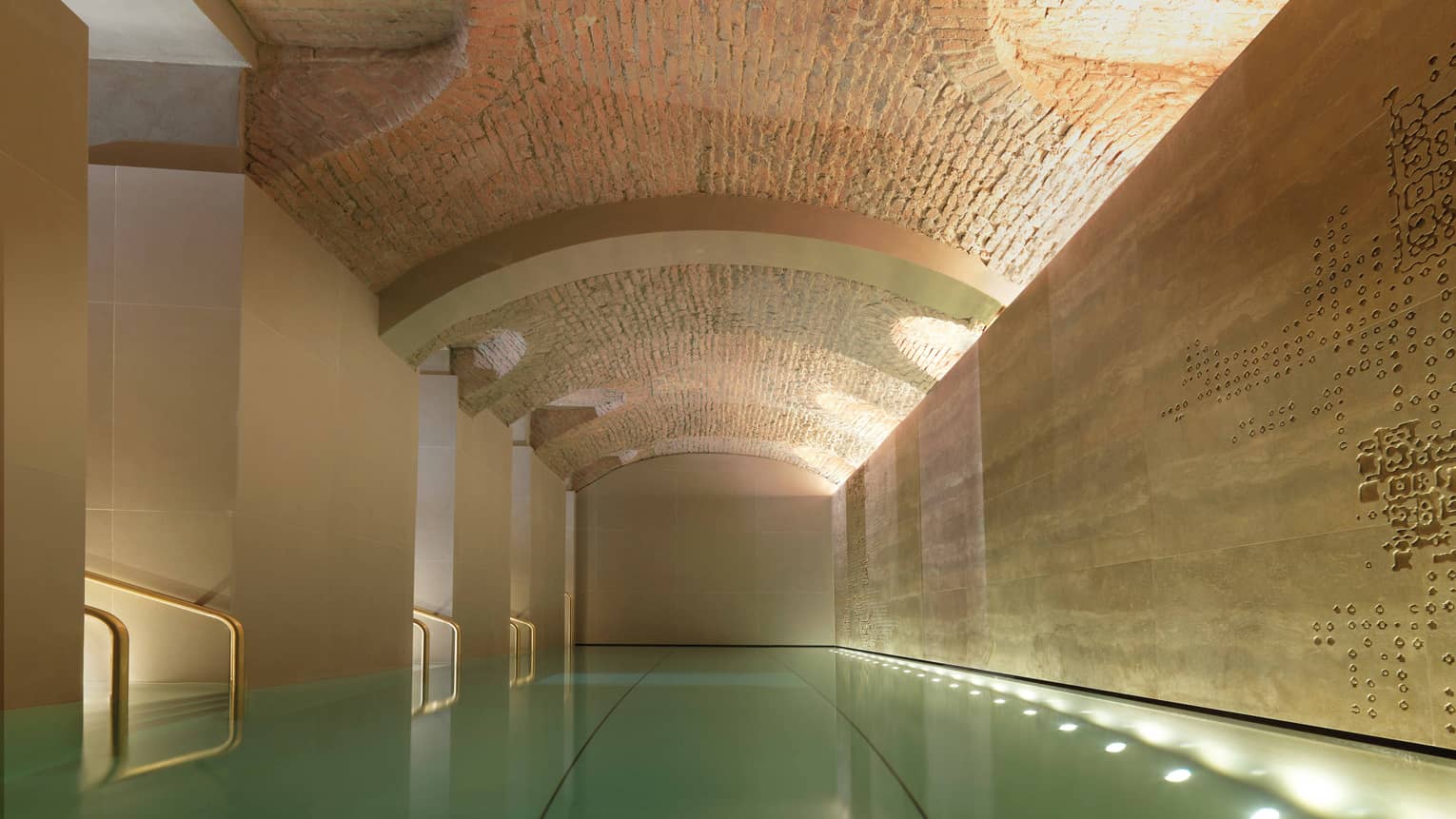Indoor lap swimming pool with gold railings under curved stone ceiling