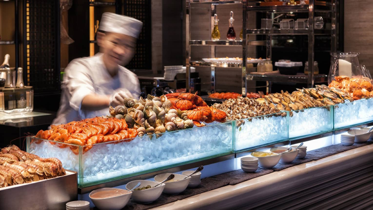 Chef reaches for snails on fresh seafood display on ice at bar