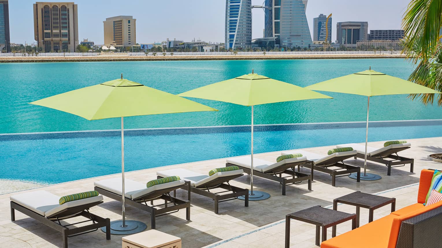 Six lounge chairs and three lime-green umbrellas in a row along infinity outdoor swimming pool