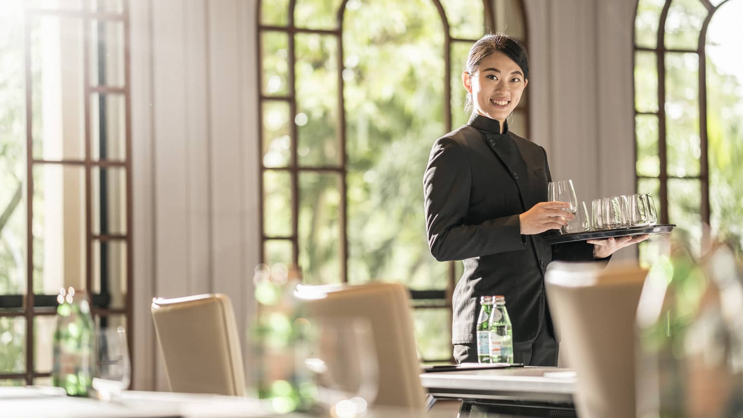 A female employee places glasses onto tables as she prepares the room for a meeting