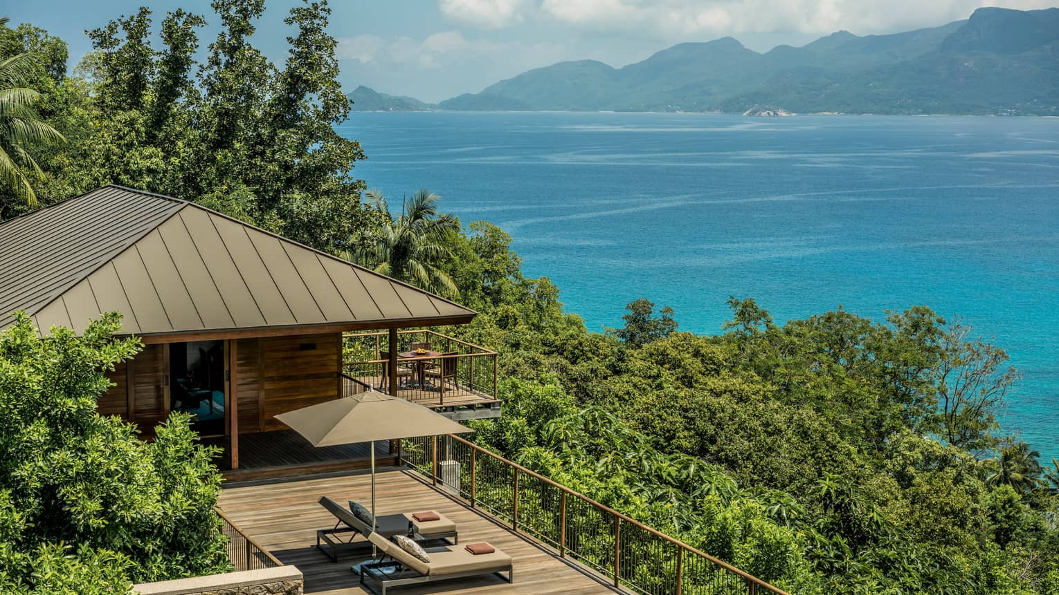 View over wood patio, villa roof on green mountain slope, blue ocean in background