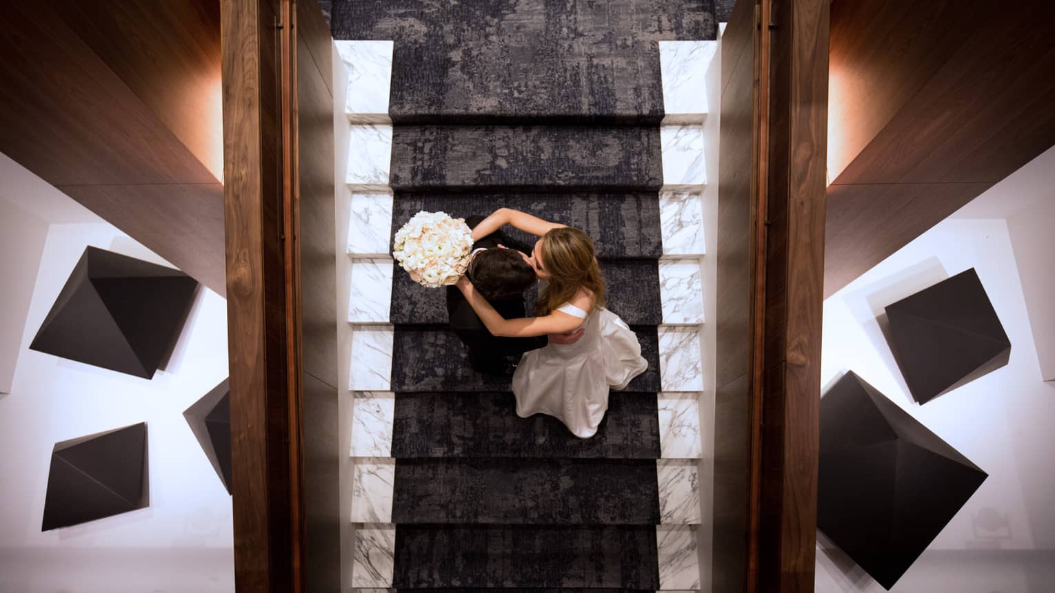 Aerial view of bride and groom kissing on modern staircase with lights