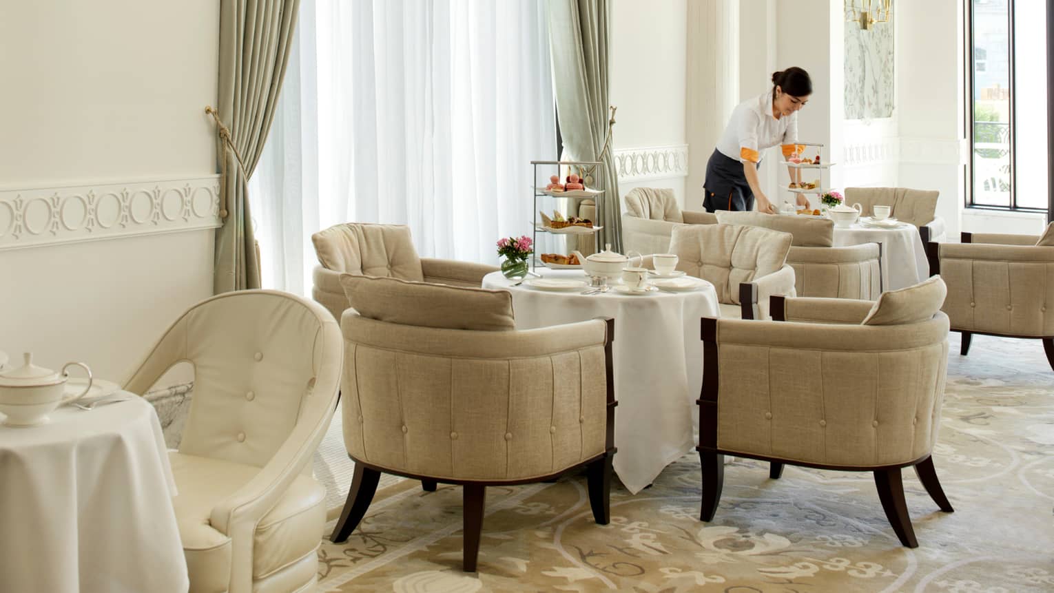 Server sets three-tiered trays with desserts and tea pots on round table in sunny Piazza dining room