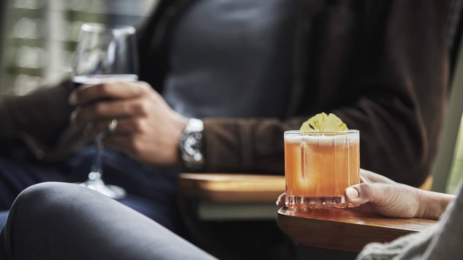 Close-up of two people sitting, holding cocktail and glass of wine