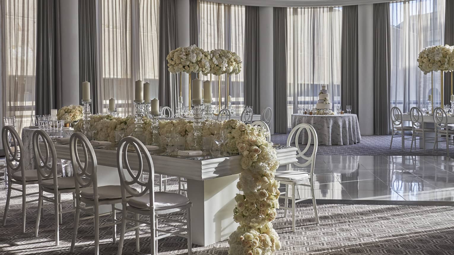 Long white rose garland over small dining table in bright banquet room