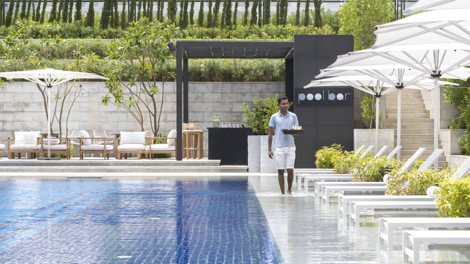 Hotel staff carries tray alongside outdoor swimming pool and sunny patio deck