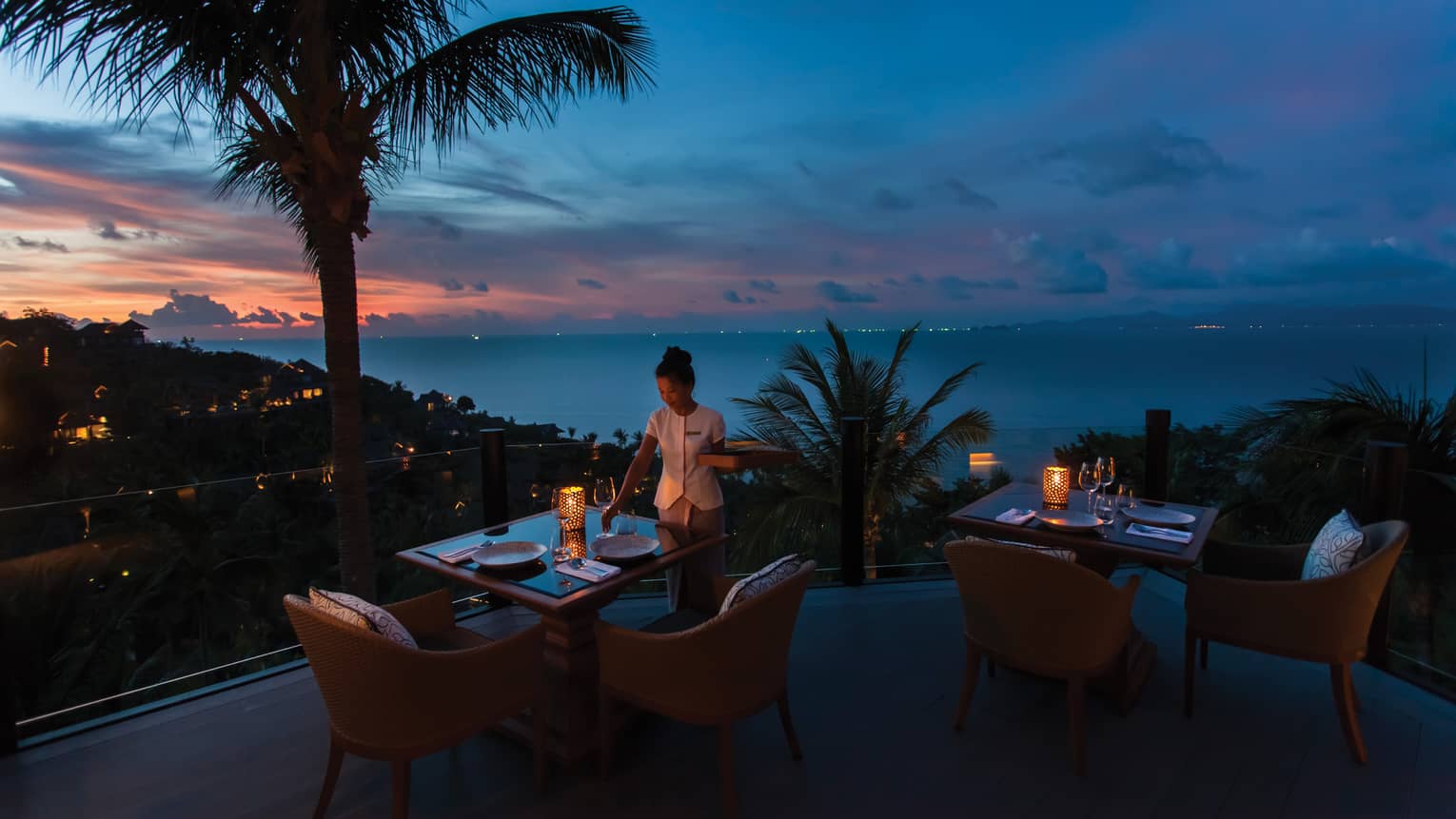 Waitstaff sets the table on outdoor terrace at Koh Thai Kitchen in Koh Samui, view of palm trees and Gulf of Thailand