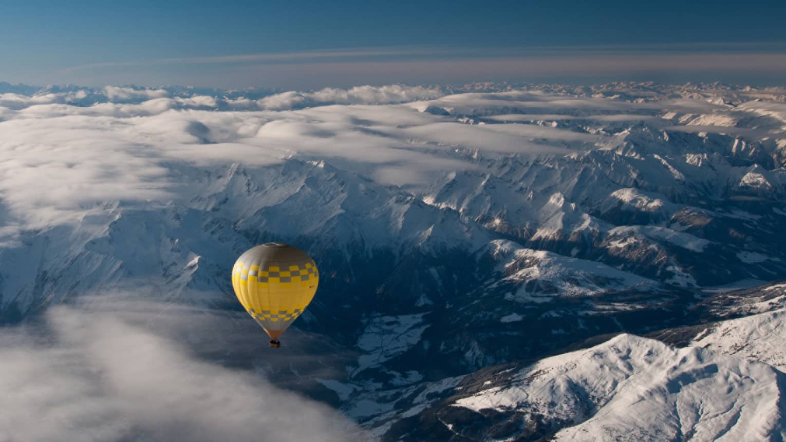 Yellow hot air balloon soaring over the snow-covered Alps