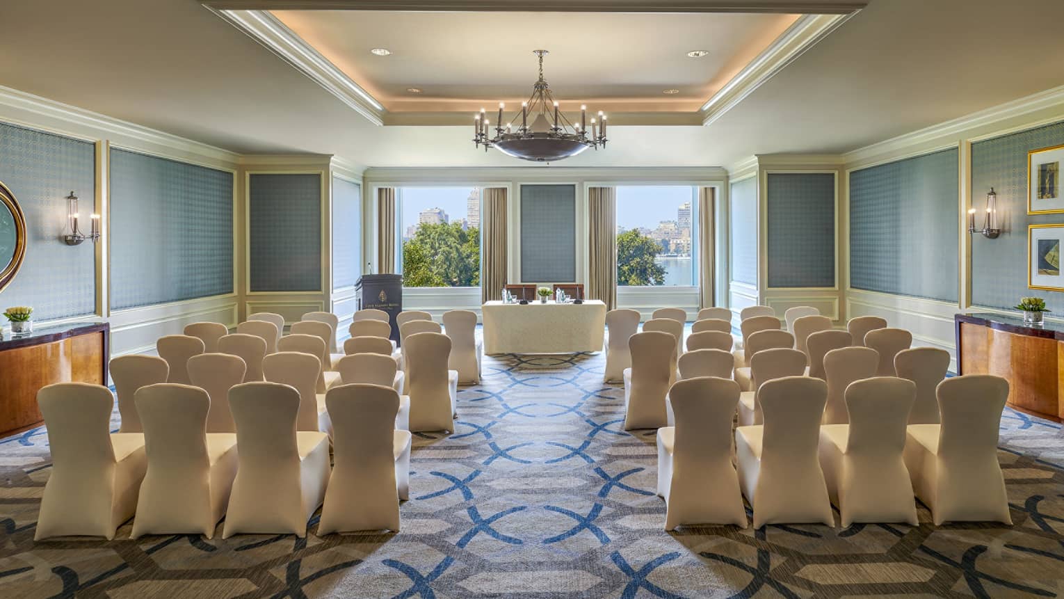 Rows of fabric covered chairs face conference table, podium and sunny windows