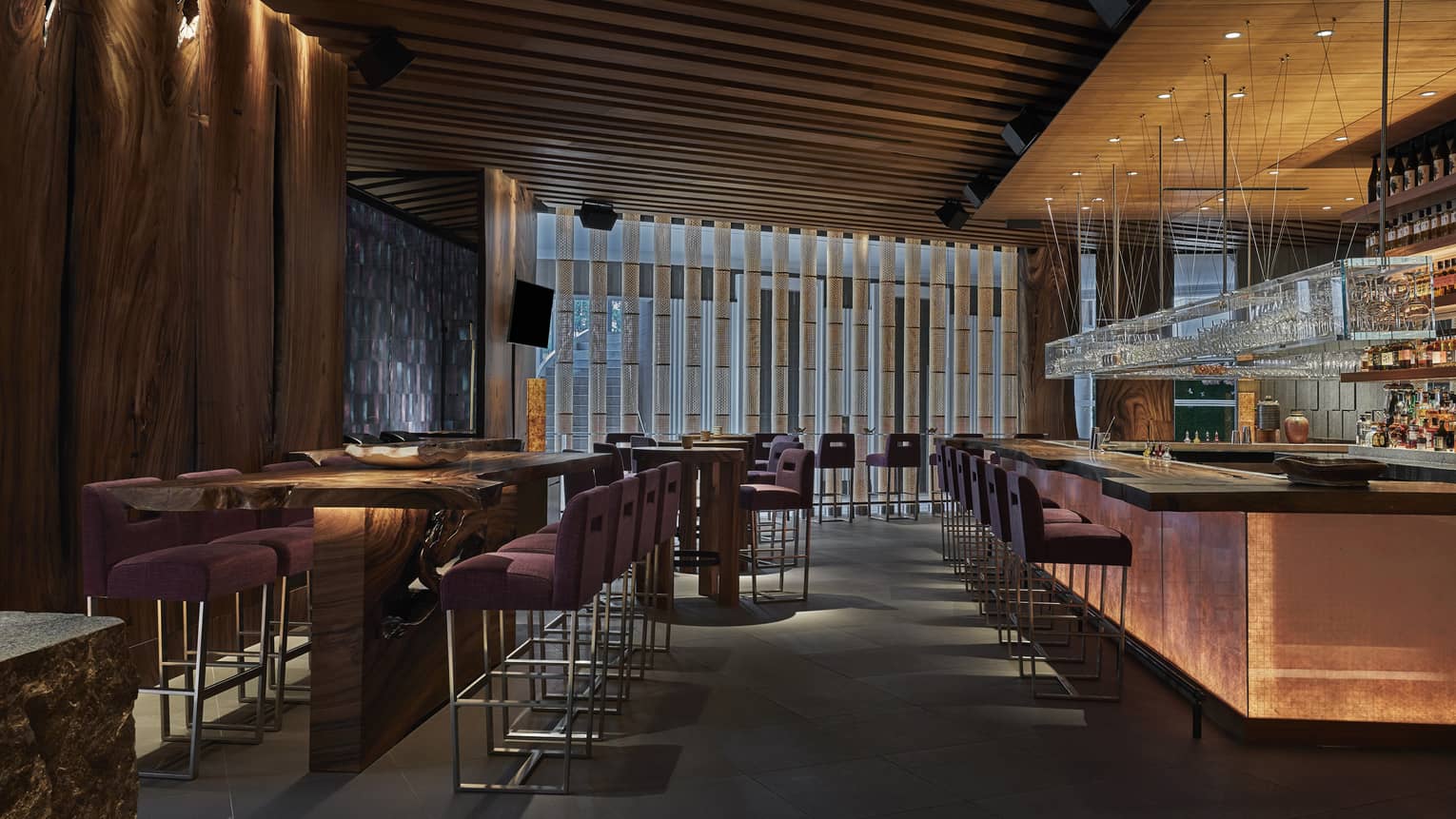 Interior of a modern dining room with wooden tables, purple upholstered chairs and a spacious bar area