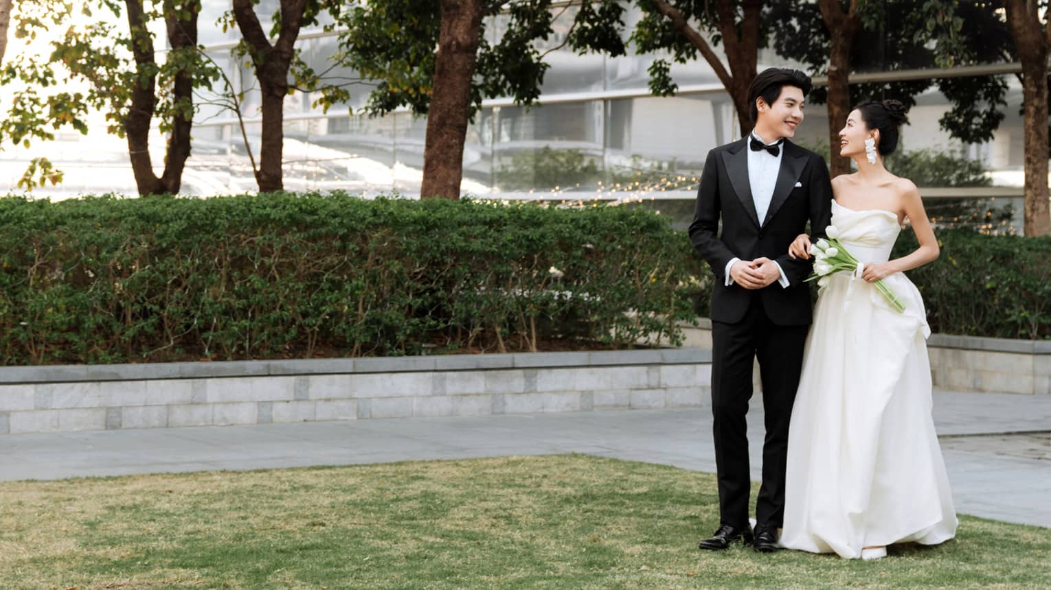 Bride and groom stand on outdoor terrace flanked by trees