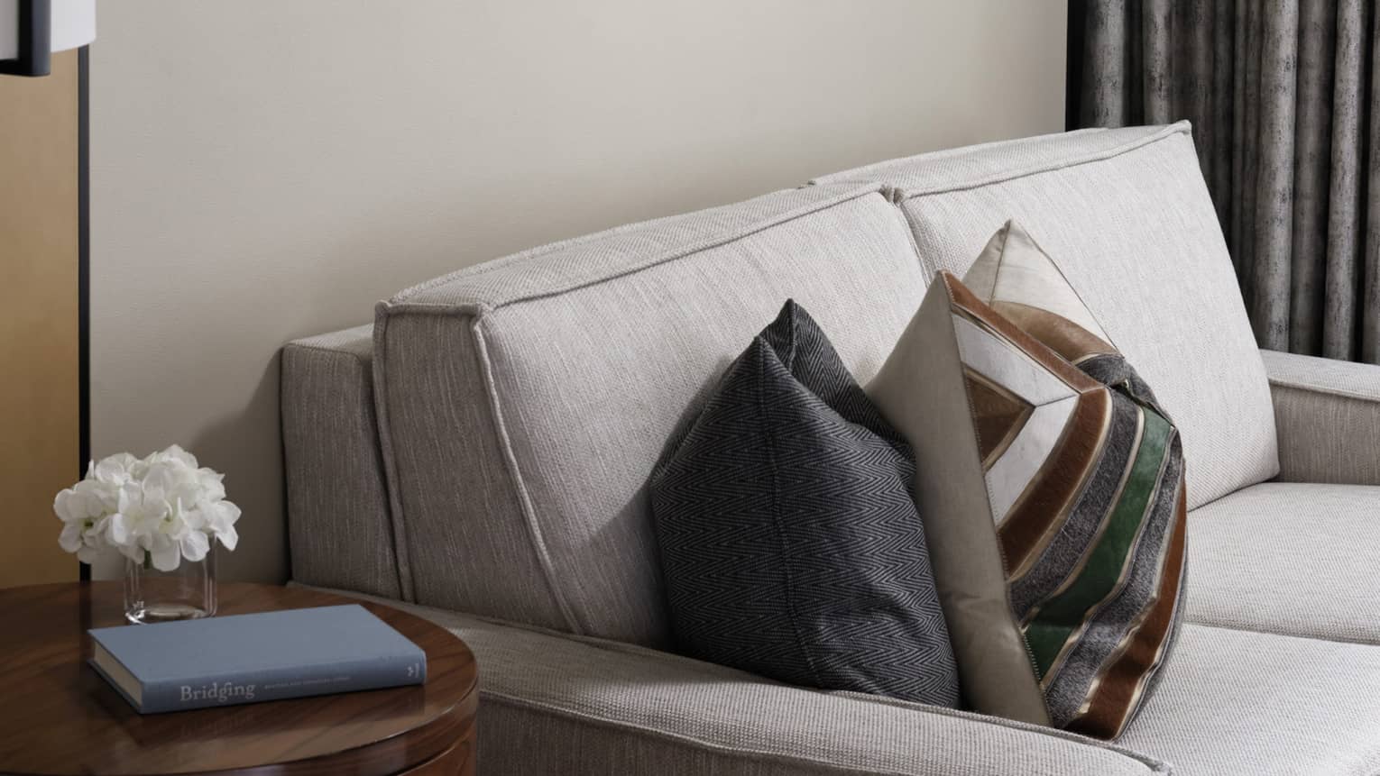 Cream loveseat, patterned accent pillows, wooden side table, wall art trio, grey curtains