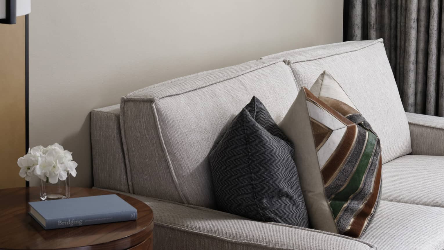 Cream loveseat, patterned accent pillows, wooden side table, wall art trio, grey curtains