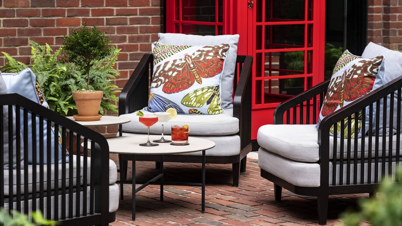 A small eating area outside with plush chairs, a red phone booth and brick ground and walls.