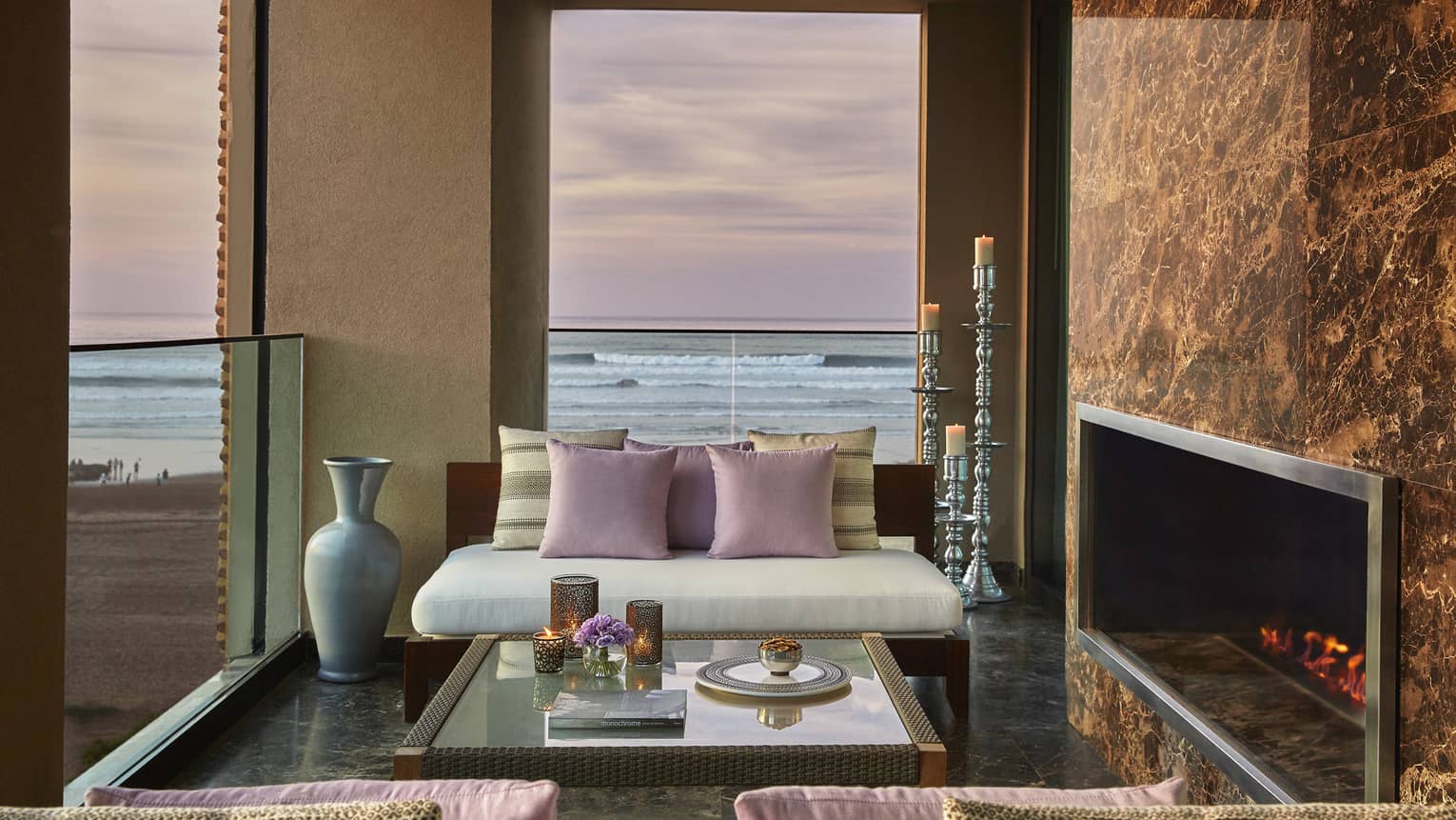 Royal Suite Ocean View white sofa, pink pillows by fireplace, under window with pink sunset, ocean
