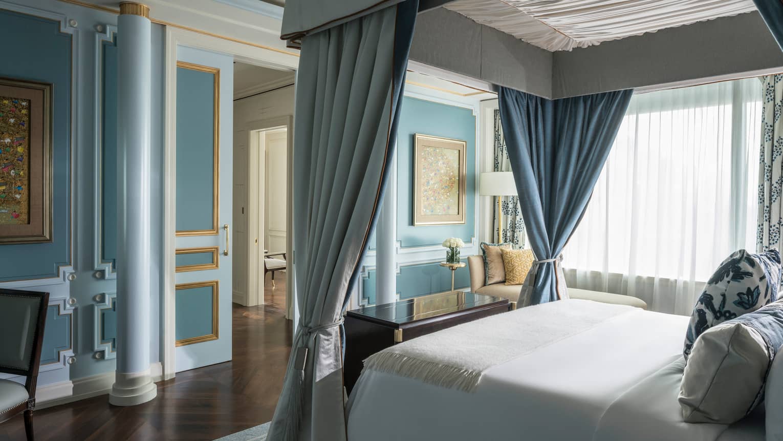 Canopy bed with white linens across from blue wall with pillar
