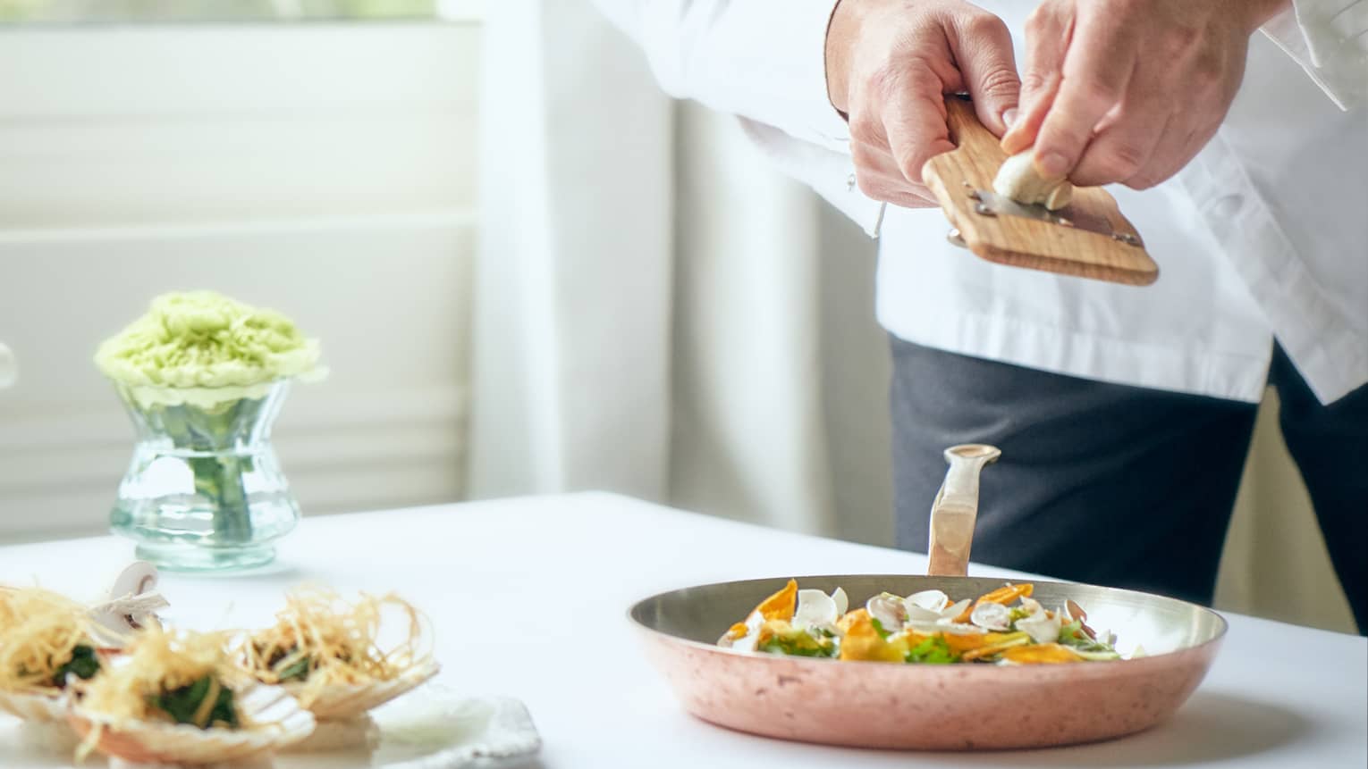 Chef grates mushroom over vegetables in pan