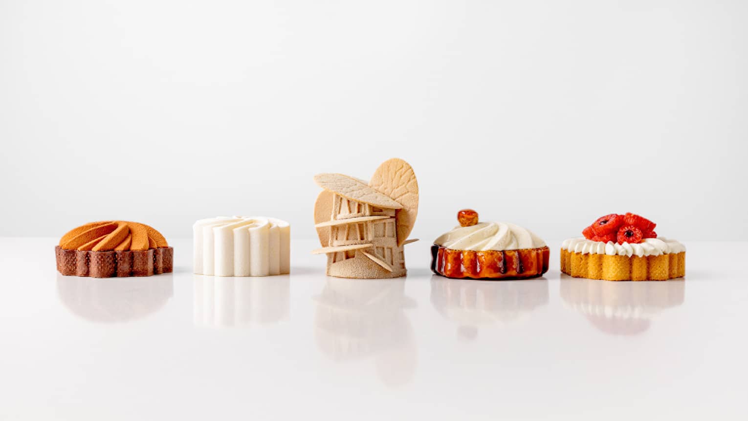 Row of five artfully prepared pastries set next to each other on an all-white backdrop