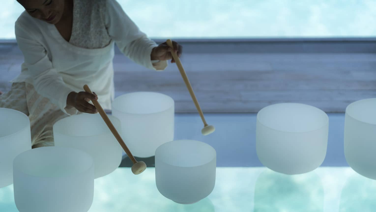 Spa staff plays various white crystal bowls with wood mallets during sound healing session