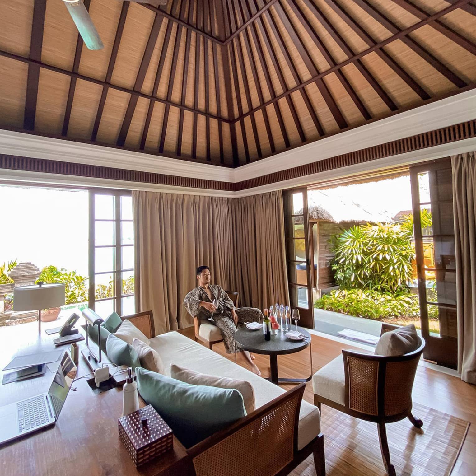 Man wearing robe relaxes in chair with wine glass in open air corner