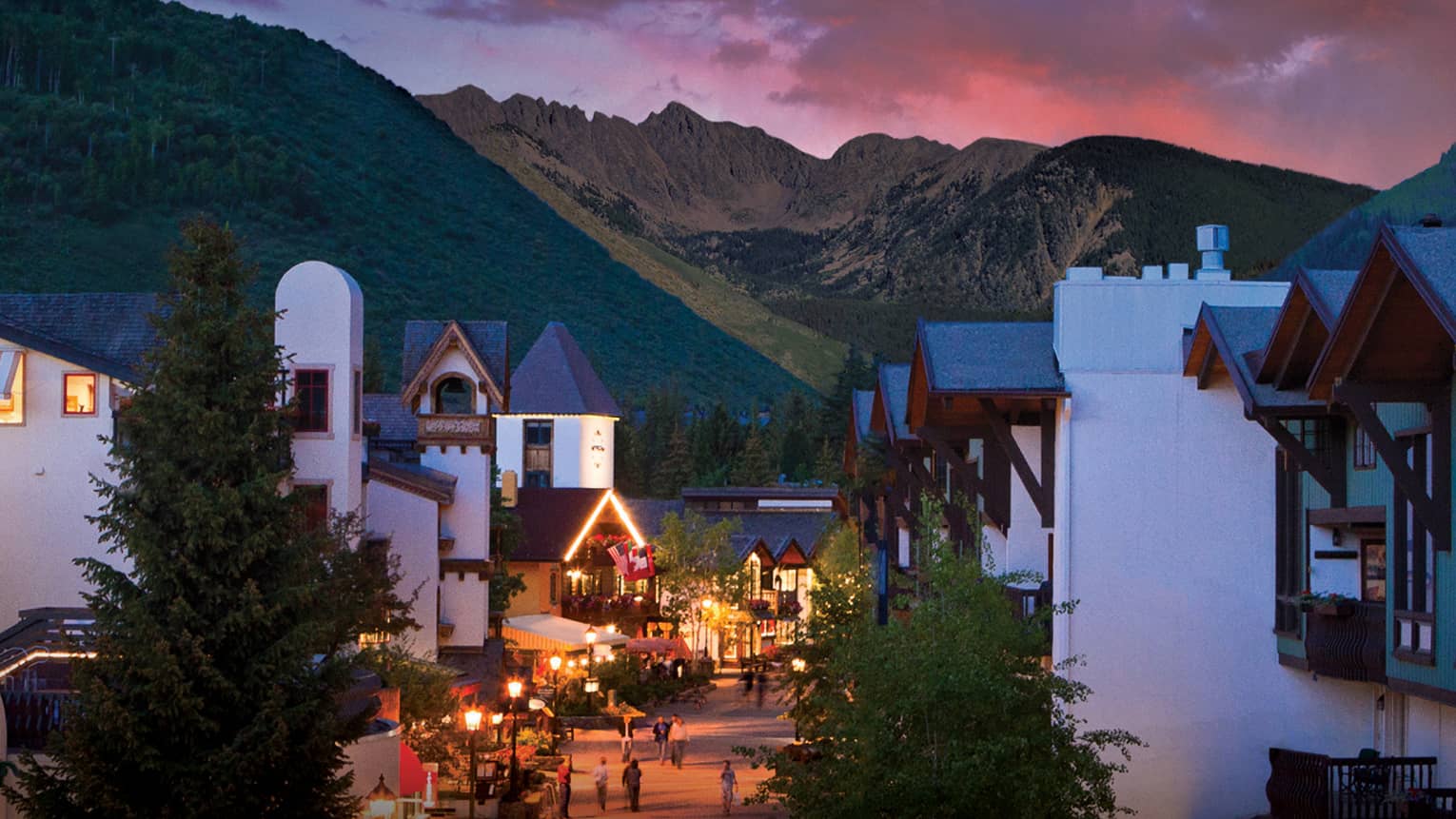 A sunset over a small village like city center with white buildings and mountains in the distance.