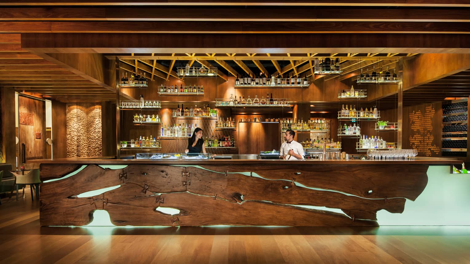 Two Grain bartenders behind rustic wood bar with lights, liquor bottles on shelf displays