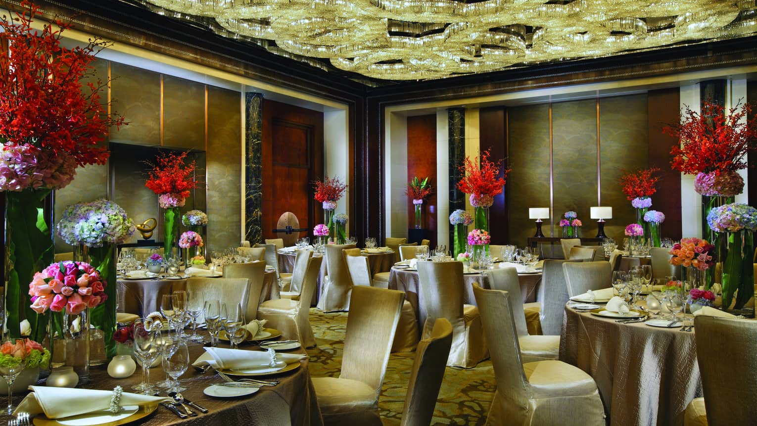Ballroom banquet tables, red flowers under ceiling with elaborate crystal chandelier design