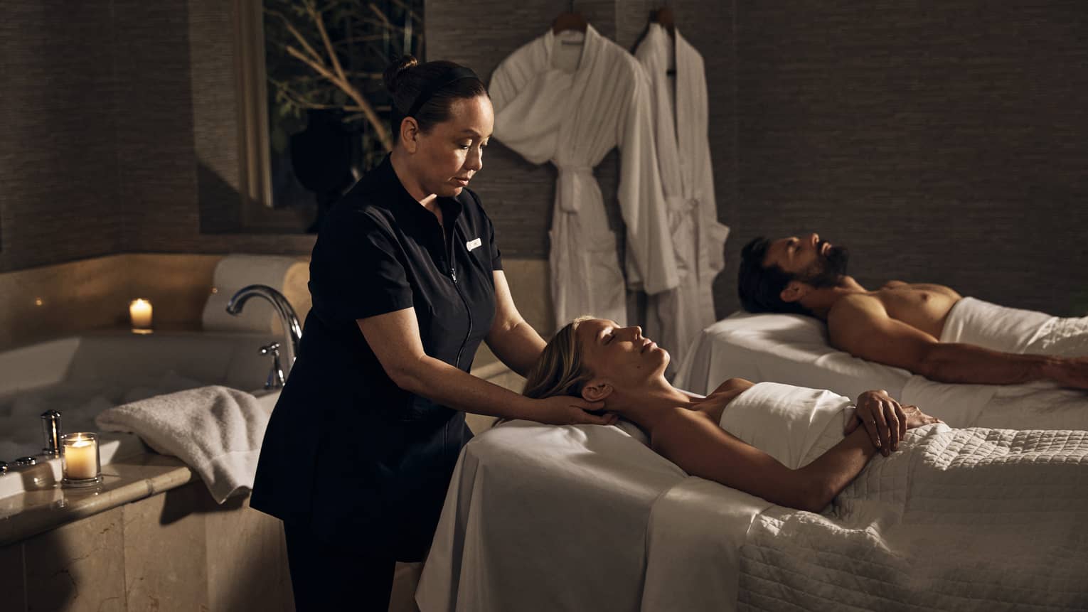 Two guests laying on massage tables in a room with a spa tub.