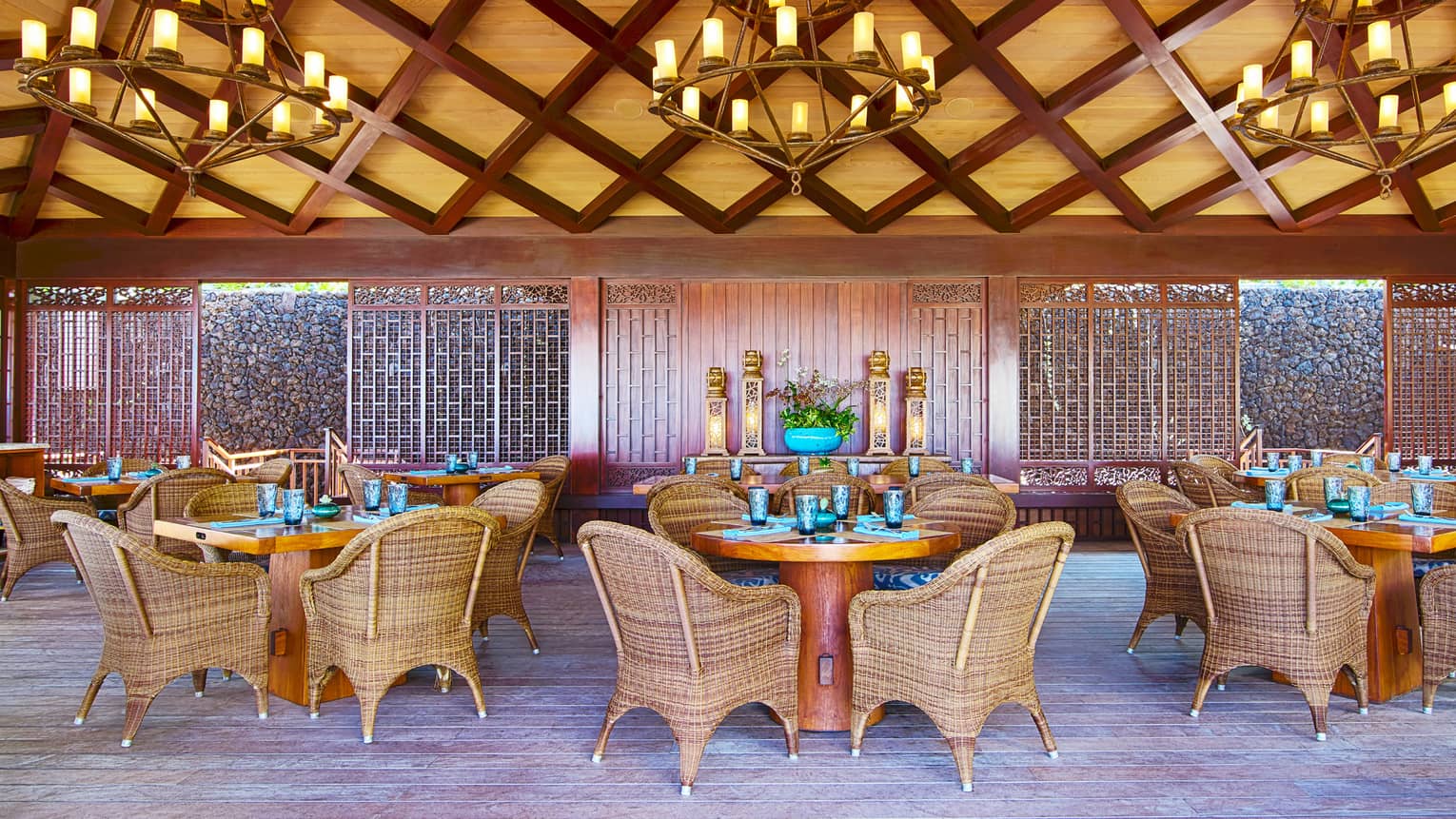 Dining area under bamboo and lattice ceiling with three chandeliers, round dining tables and wicker chairs