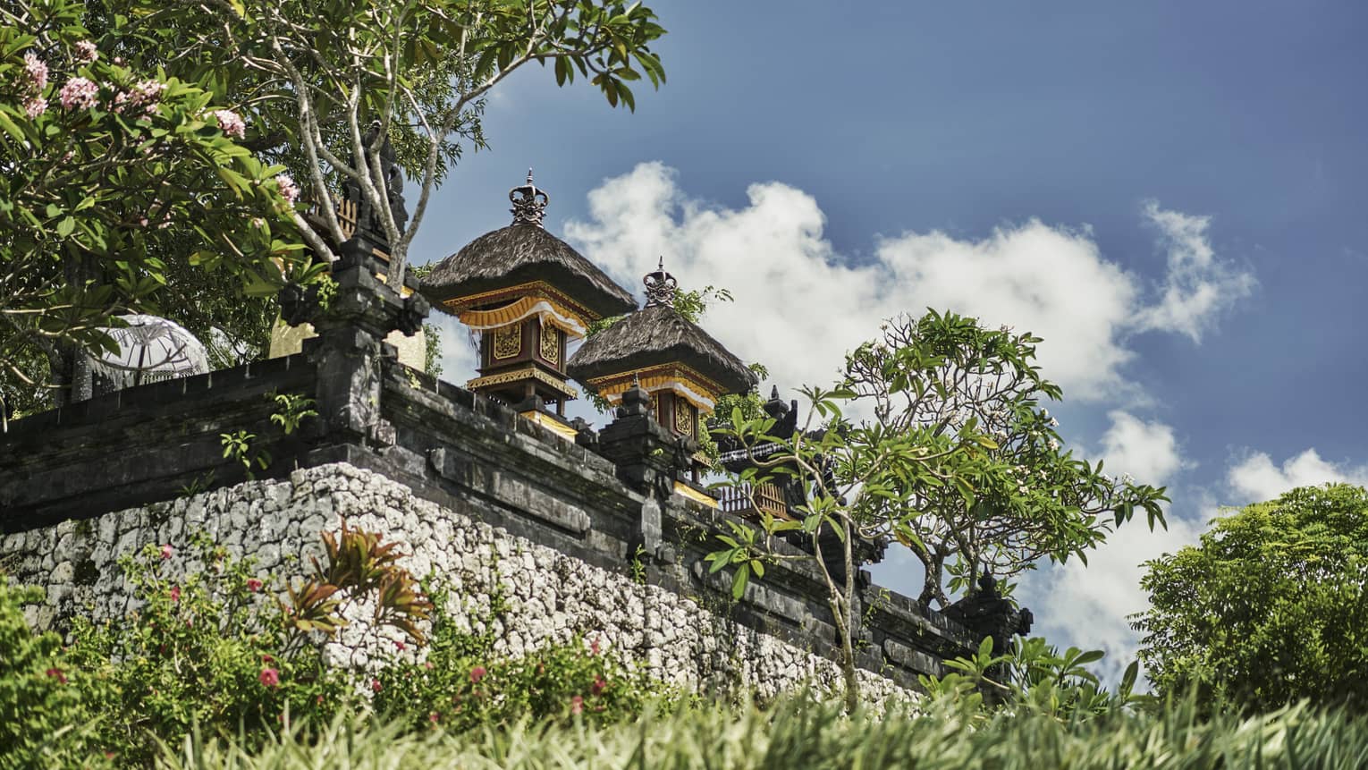 Exterior view of resort temple with stone wall, posts and carvings, tropical trees