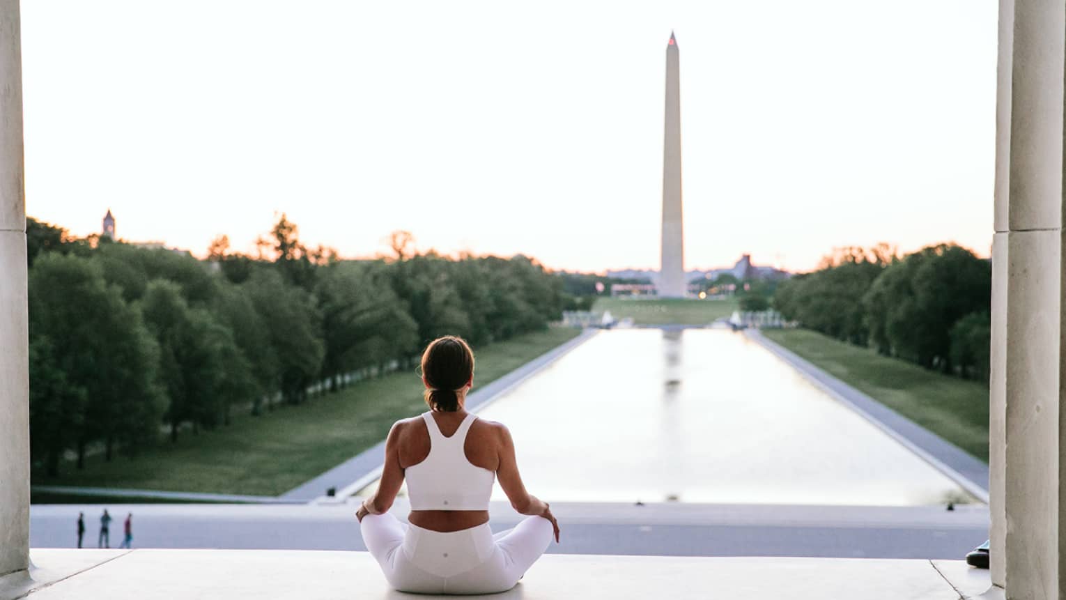 A woman in workout clothes is sitting and looking at the Washington Monument.