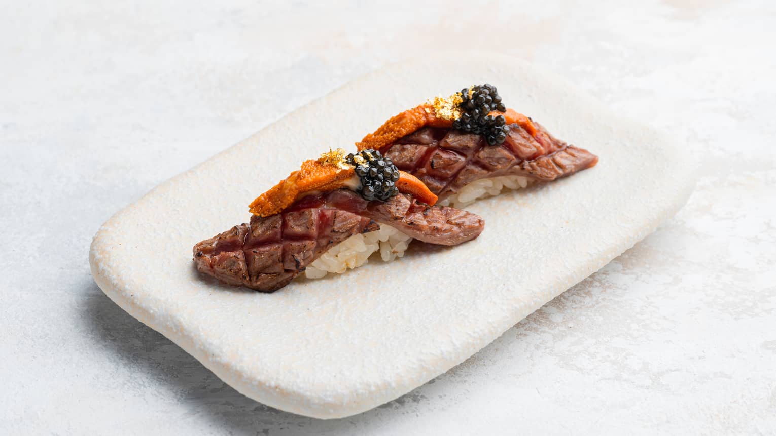 Wagyu, Sea Urchin and Caviar Nigiri on rectangular white dish
