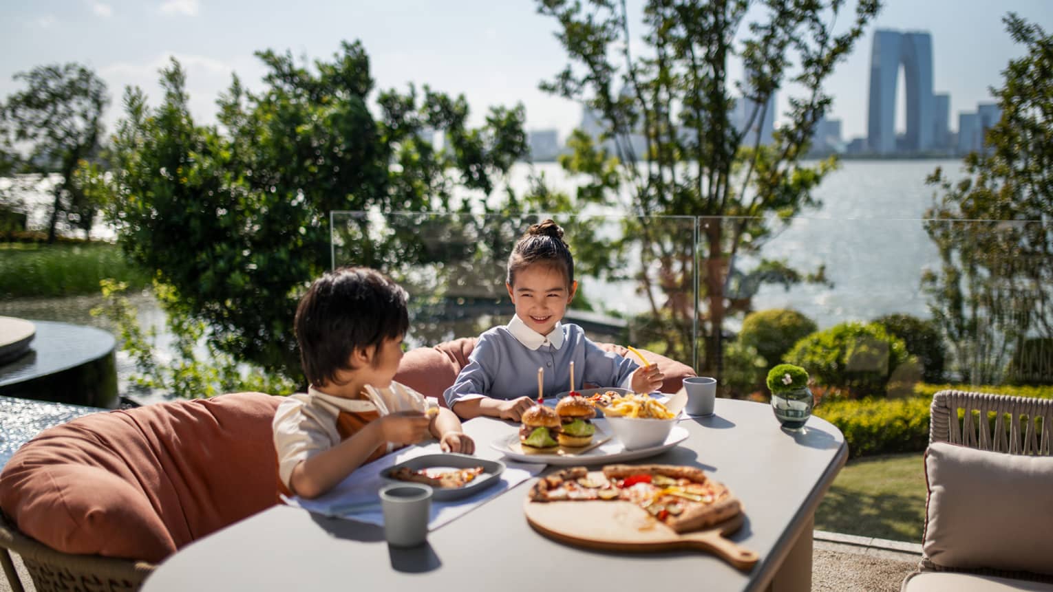 Young boy and girl dine at outdoor restaurant table with lake and city view