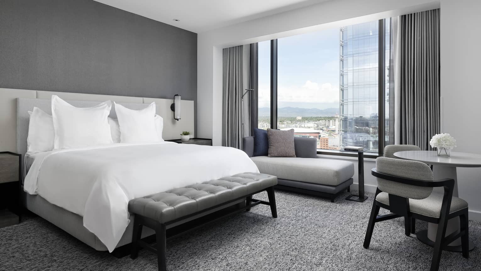 Hotel room bed, bench, small table and chaise by floor to ceiling window