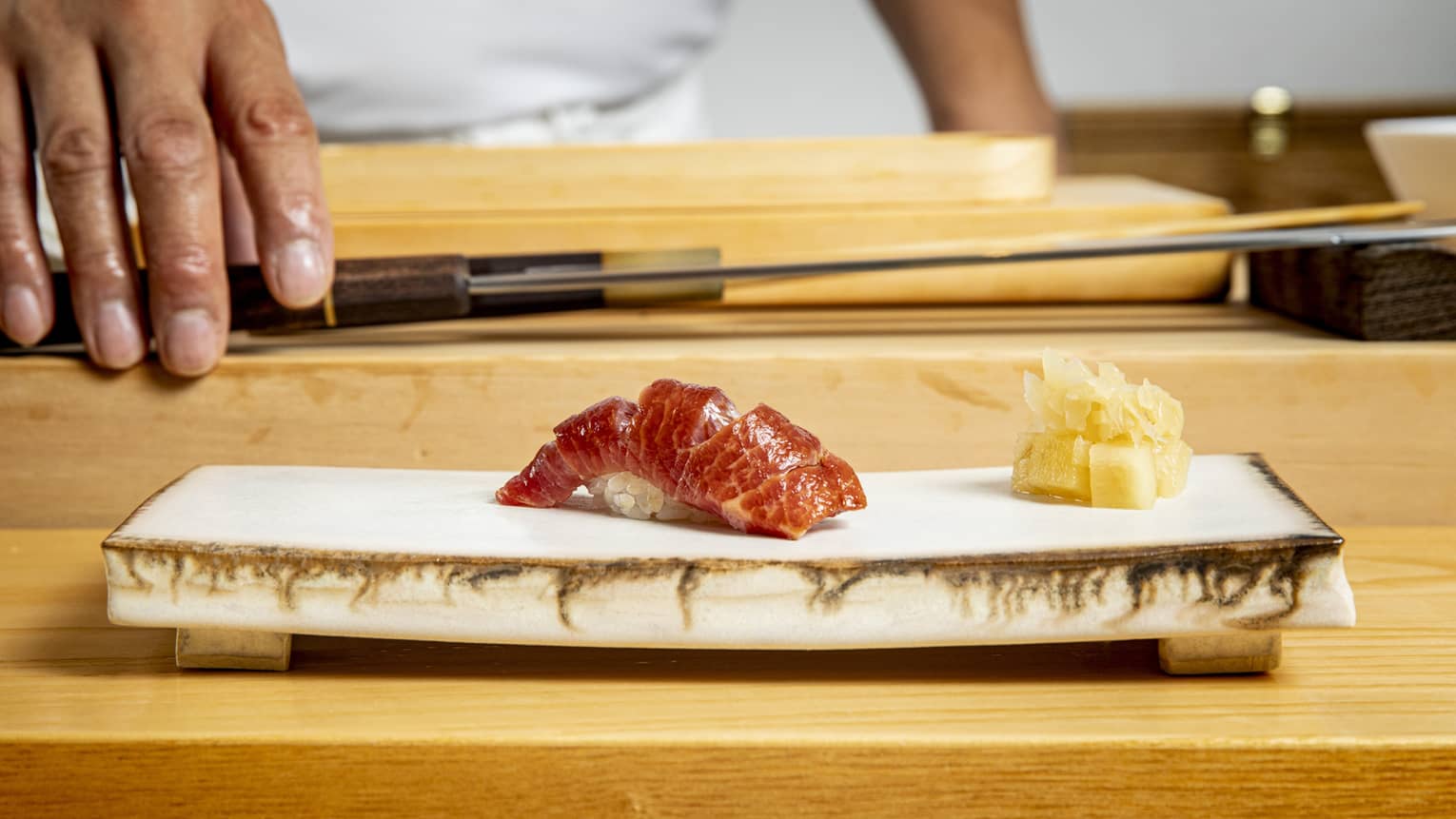Edomae sushi on a modern stone plate, with a chef and chef's knife in the background
