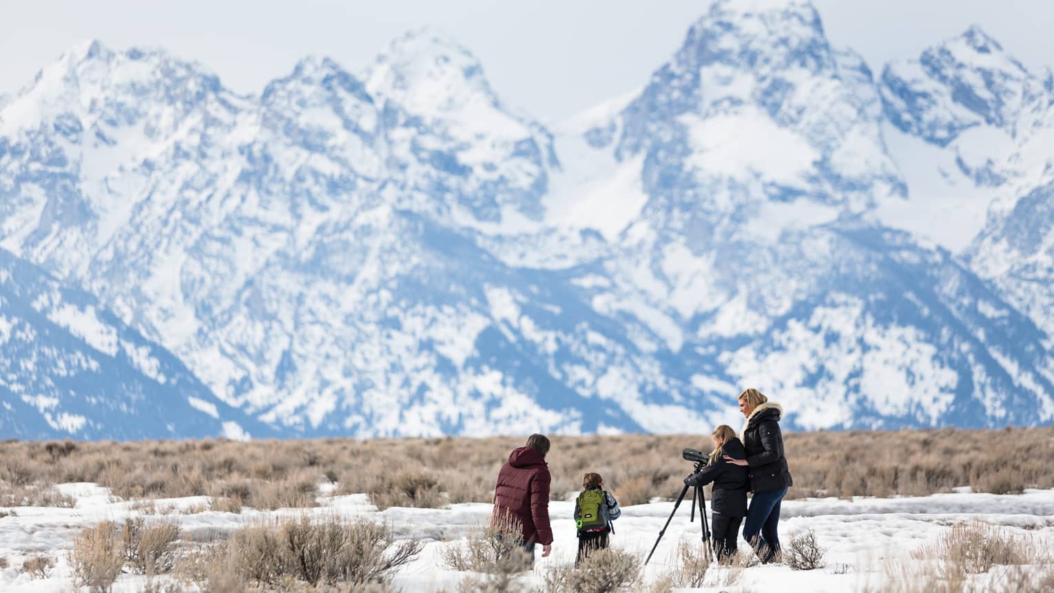 Family in snowy field with camera on tripod pointed at towering mountains