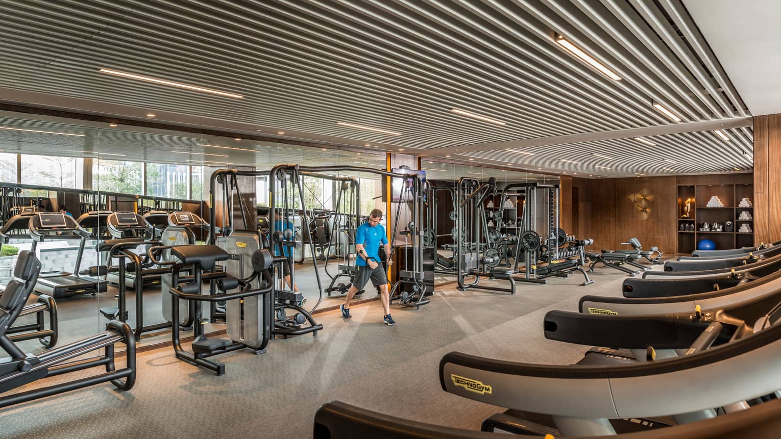 Man pulls weights machine in large Fitness Centre by mirror reflecting treadmills