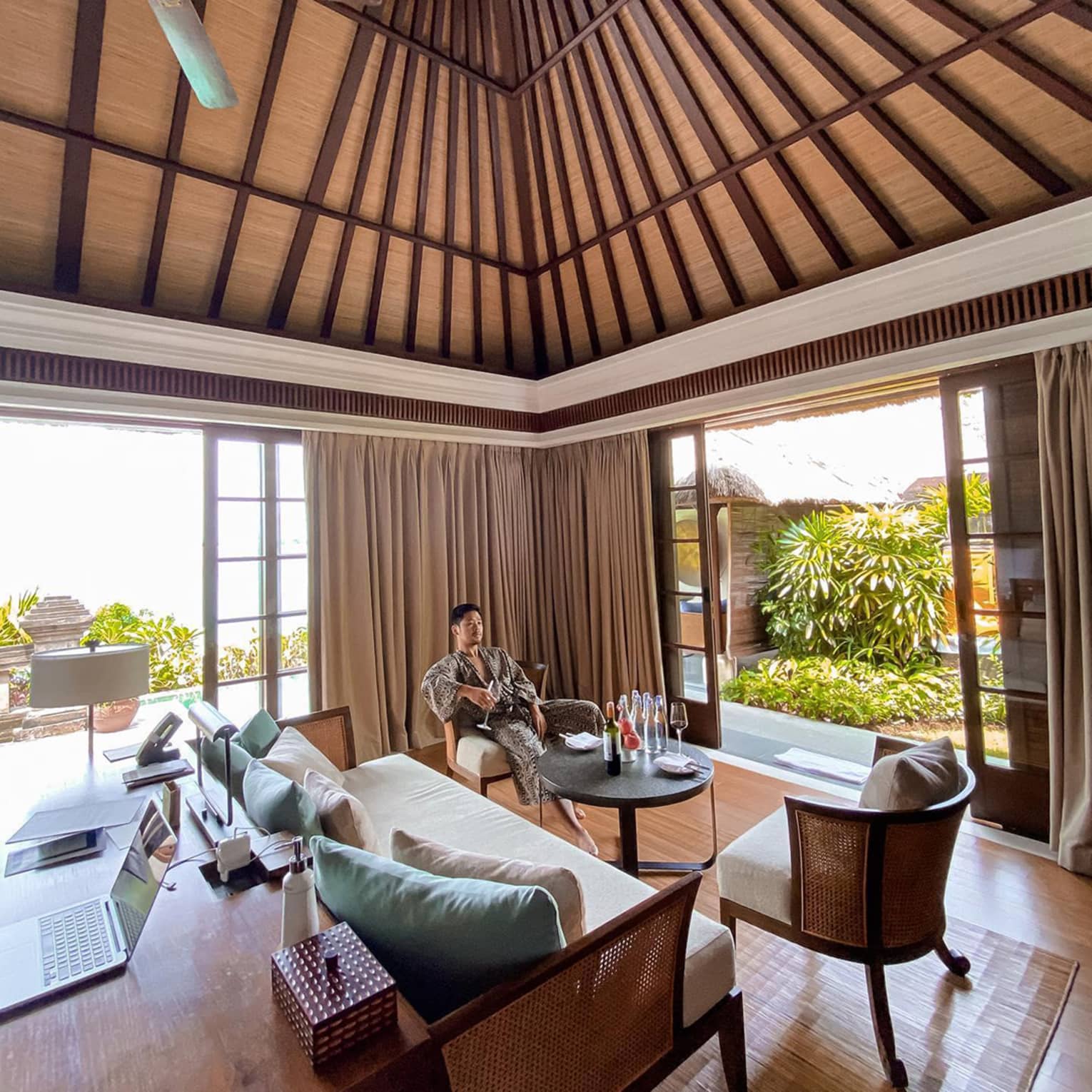 Man wearing robe relaxes in chair with wine glass in open air corner