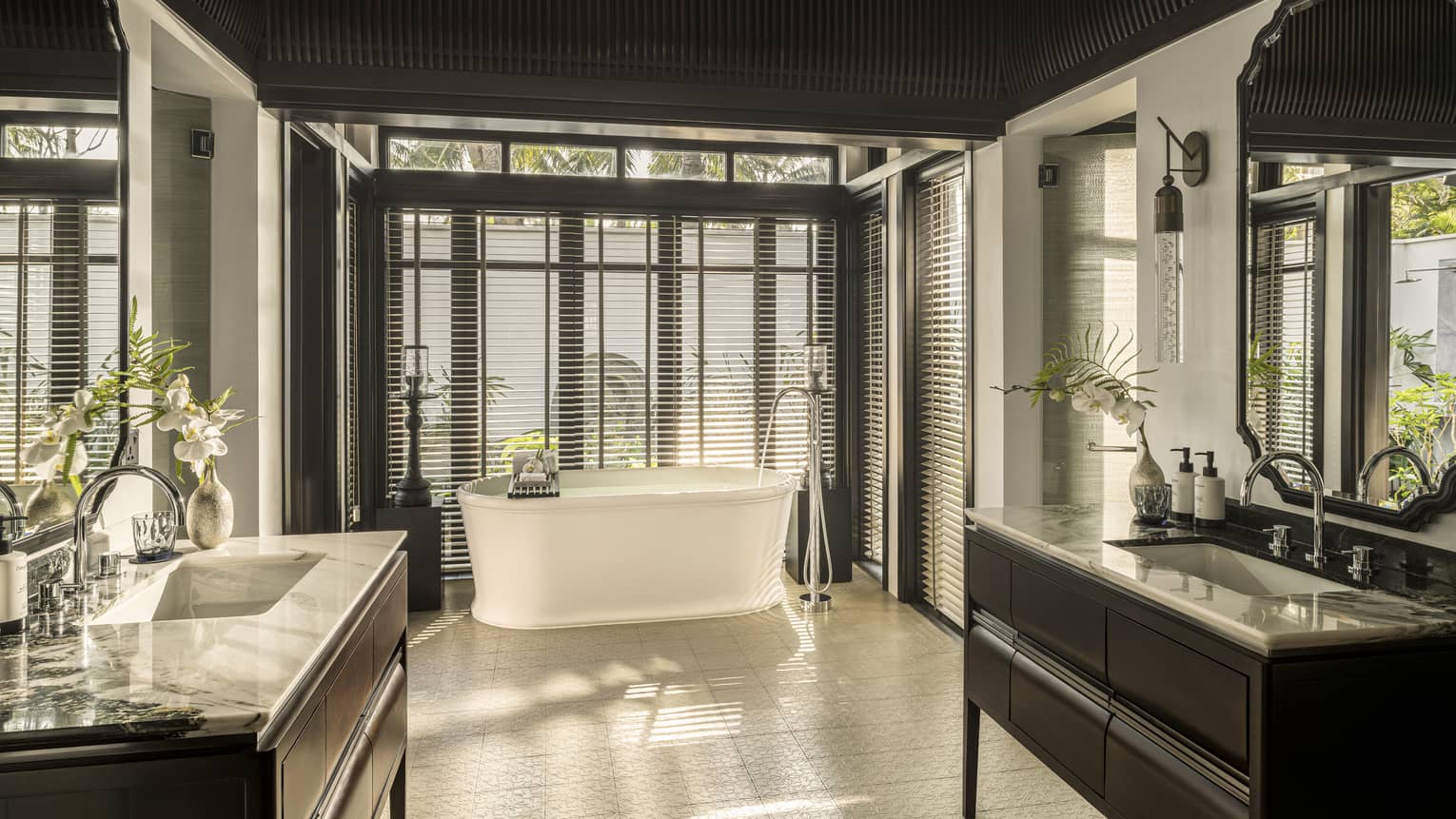 Large luxury bathroom of resort villa, featuring a vanity on each side of the bathroom and a freestanding tub next to a wall of windows