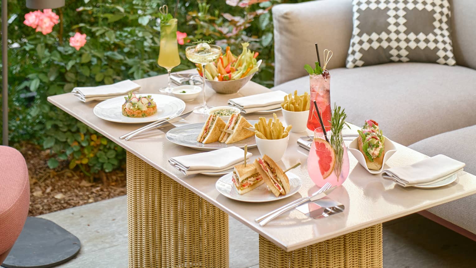 An outdoor table topped with various sandwiches, salads and colourful cocktails