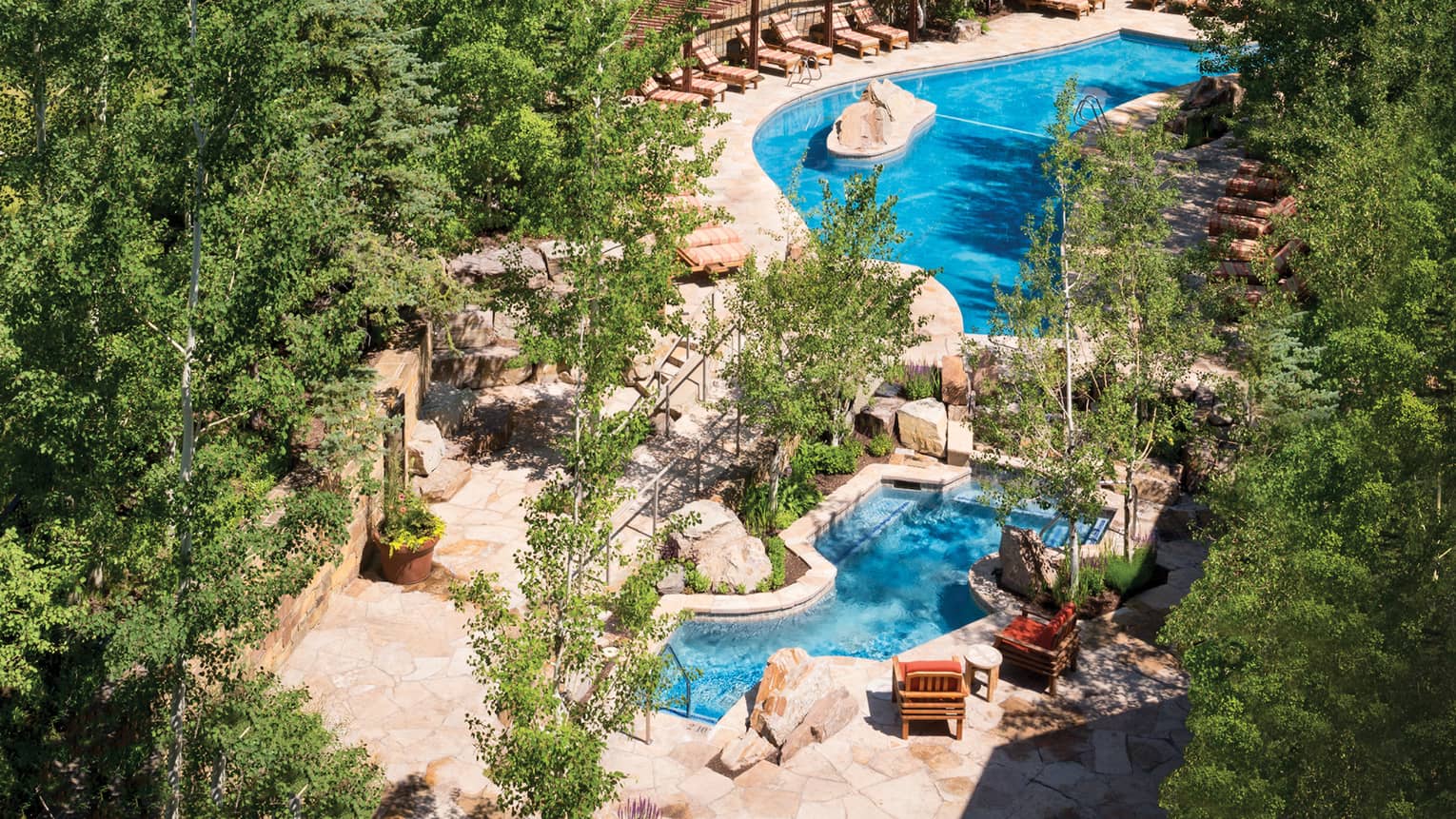 Aerial view of winding outdoor swimming pool, deck with lounge chairs surrounded by trees