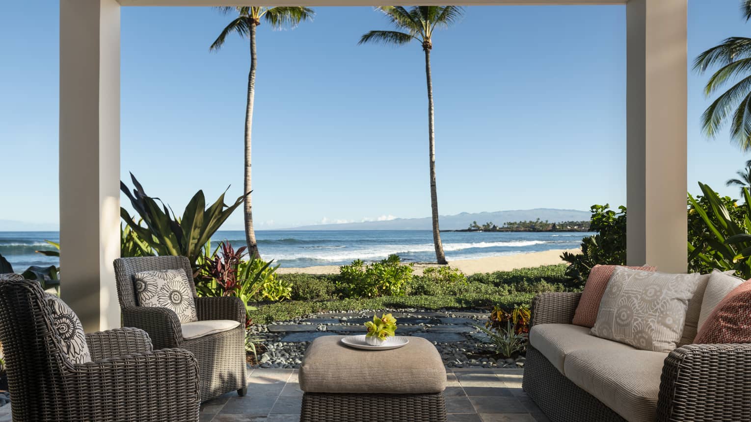 Covered lanai with dark wicker sofa and two matching arm chairs, ottoman, beach view